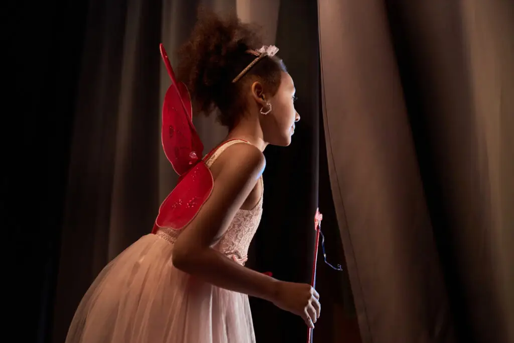Waiting to perform at dance eisteddfods - a young girl standing behind the theatre curtain dressed as a fairy