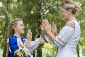 Woman claps hands with daughter dressed in Ukrainian national dress. Represents defiance, like Ukraine's red character shoe.